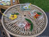 Four glass snack trays with floral designs, each paired with a glass cup placed on a round wicker table outdoors.