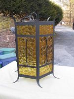 Full view of the vintage Spanish Gothic wrought iron hanging lamp with amber textured glass panels. Shows overall design and condition including one missing glass panel.