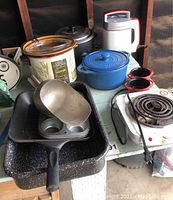 Overall view of the kitchenware items grouped together showing the assortment of pots, pans, and appliances on a table.