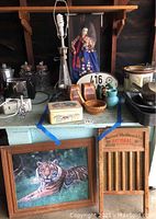 Overall lot view featuring Korean doll in glass case, lamp base without shade, wooden bookends, car tags, laundry washboard, and framed tiger print