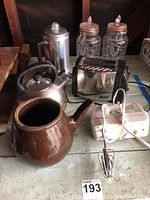 Photo showing Hamilton Beach electric hand mixer, two tin kettles, silver toaster, two glass jars, brown ceramic teapot, and French press coffee maker on wooden shelf.