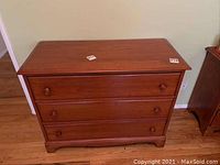 Front view of wooden 3-drawer dresser showing design, drawer fronts with knobs, and overall condition.