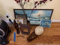 Full room view showing framed paintings, wooden sculptures, bowls, and red flowering branches grouped together on hardwood floor.