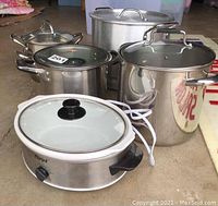 Photo of stainless steel kitchen pots in various sizes with glass lids plus two Parini electric food warmer/steamer units in front.