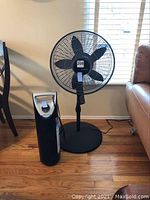 Photo showing both the Thera Pure air purifier tower and Lasko floor fan side by side on hardwood floor near a window.