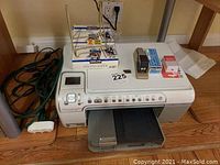 Full view of HP Photosmart C5250 printer with green extension cord and miscellaneous supplies on wooden floor beneath a desk.