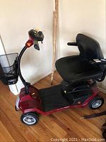 Side view of red Shoprider scooter showing frame, four wheels, mesh basket and swivel seat