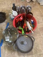 Photo showing two gray pots with lids, three stainless steel coffee travel mugs, two white coffee cups, and a red bowl filled with various kitchen utensils.