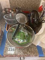 Miscellaneous kitchen items on countertop including glass bowls, strainer, green decorative bowl, electric hand mixer with beaters, and Minnie Mouse salad tongs.