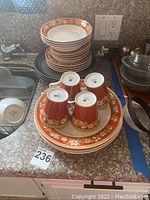 Overview of stacked bone china dishware including cups, plates, and bowls with orange floral design