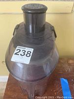 Juicer top part with black plastic feed chute and plunger, showing MaxSold lot number sticker on top.