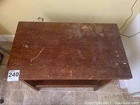 Top down view of the small wooden utility table's rectangular top surface showing scratches, marks, and surface wear.