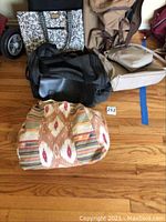Image showing four assorted bags on floor: black and white floral tote, tan duffle, black rolling suitcase, southwestern fabric duffle.