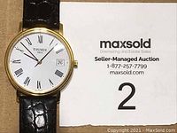 Front view of watch face showing Roman numerals, date display, and gold-tone case.