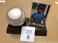 Photo showing autographed baseball mounted on wood stand beside signed baseball card in display case.
