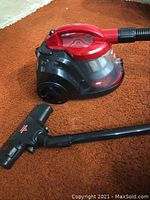 Red and black Bissell Zing canister vacuum cleaner on brown carpet with hose, wand, and floor brush attachment visible.