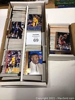 Photo showing a box filled with multiple stacks of basketball cards, with cards visible featuring players in action such as shooting or dunking.