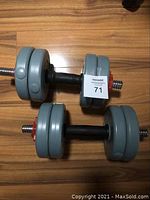 Two adjustable dumbbells with gray weight plates and red spinlock collars on wood floor.