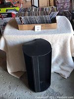 Box of approximately 60 assorted music CDs on a covered table, with a black rotating CD holder in front.