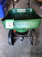 View of the green Scotts seed tray with large black wheels below, showing the brand logo and seed measurement guide.