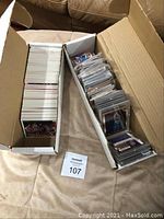 Two open cardboard boxes on fabric surface, one with loose cards and one with sleeved cards