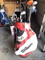 Red and white Wilson Staff golf carry bag with golf clubs inside seen from front angle.
