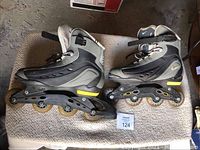 Pair of black and gray Nike inline roller blades on beige carpet with yellow accent details in Nike logo and wheel frame, size 11 USA.