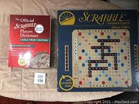 Deluxe Scrabble crossword game in original box with turntable base, next to red-covered Official Scrabble Players Dictionary Large Print Edition by Merriam Webster.
