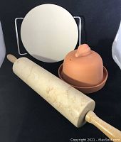 Full view of marble rolling pin, baking stone on metal stand, and terra cotta covered dish.