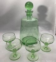 Full view of green etched glass decanter with round stopper and four matching glasses arranged around it