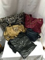 Overall lot showing five handbags in different colors and styles including leopard print, red studded, tan textured, and two black leather bags