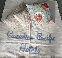 Photo of cream Kenwood wool blanket with blue 'Canadian Pacific Hotels' script and three assorted throw pillows.