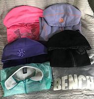 Overview of five folded hoodies showing brand logos and visible features like stitching, zipper, and collar details.