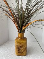 Front view of glazed square-shaped pottery vase with embossed circular and floral patterns and artificial flowers.