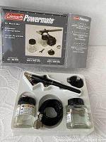 Photo of opened Coleman Powermate Air Brush Kit showing airbrush, air hose, multiple jars with covers and adapters arranged in a plastic tray, and box in background.
