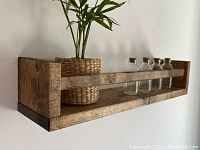 Side angled view of wooden wall shelf holding small plant and spice bottles, showing wood grain and walnut stain.