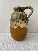 Full frontal view of the jug showing rust brown lower matte glaze transitioning to brown and white lava glaze on upper half and handle.