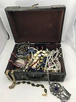 Opened keepsake box showing various vintage costume jewelry items inside including necklaces, bracelets, brooches, and rings.