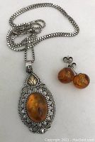Photo of sterling silver necklace with amber oval pendant and matching amber round stud earrings on a white background.