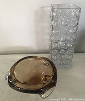 Overview of the two glass pieces together: one tall clear glass vase with circular bubbles and one amber glass bowl with curved organic form.