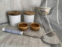 Full six-piece set showing two white ceramic canisters with wooden lids, two small wooden bowls, handmade pottery bowl, and ceramic-handled spatula with decorative handle.