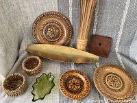 Overview of 9-piece boho decor lot including wooden carved plates, brass tray on legs, woven holders, green glass dish, reeds, and wooden square piece.