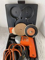 Orange and gray Black & Decker electric drill with power cord, sanding attachment, multiple sanding discs, all inside original black molded plastic carrying case