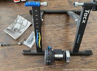 Indoor bike trainer frame on wooden floor with accessories and manual, showing Tacx branding and Cycletrack text.