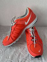 Side angle view of bright reddish-orange Nike Training running shoe showing white swoosh logo and gray interior lining with laces tied.