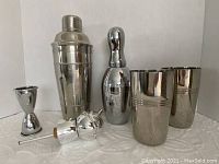 Full cocktail shaker, small engraved bowling pin shaker, two julep cups, jigger, and three liquor pour spouts including one stopper