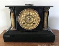 Front view showing black case with gold decorative round clock face and two gold fluted columns.