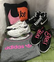 Nike white running shoes, Nike black high tops, Vans black high tops with pink laces, Adidas gray pullover with pink logo, Nike black pullover with large swoosh logo, and Nike pillow