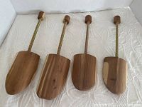 Set of four wooden shoe trees laid out side by side on a white surface showing the wood grain, metal spring, and wooden knobs.