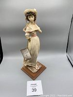 Front view of the Pink Lady figurine showing detailed bonnet, facial features, gown with pink sash, and wooden base.